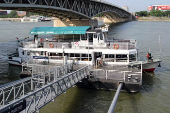 a white public boat anchored at the grey Arpad Bridge