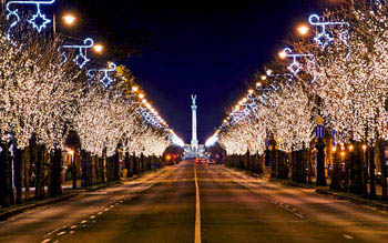  trees lining Andrassy ave, with festive lighting at night, the column at Heroes sqr. in the distance