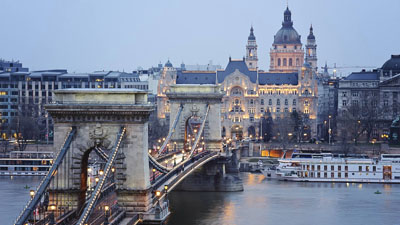 panoramic view of the Chain bridge , a white ship, the Gresham Palace and the Basilica at dusk