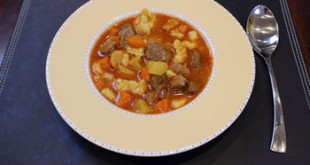 goulash served in a round plate placed on a dark brown place mat