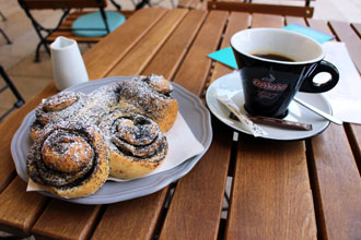 chocolate snails on a palte and coffee in a black cup on a wood terrace table