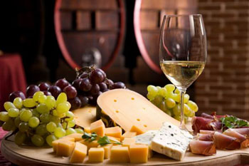 a half glass of white with bunches of grape and chunks of cheese on a wooden table