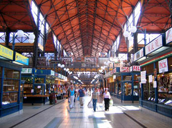 shoppers and tourists walking on the ground level of the market, under an iron structure roof