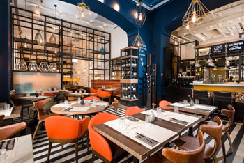 small round and square wooden tables with orange leather upholstered chairs in Bistro Fine