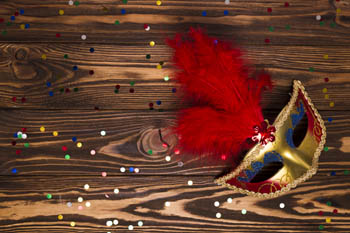 a red and gold carnival mask on a wooden surface