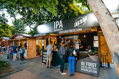 3 people at the wooden booth of IPA Beer House beer maker, under the canopy of platan trees