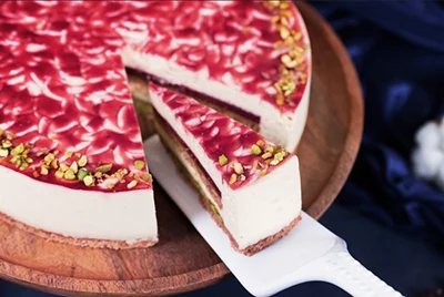 a slice of red and white cake cut from the whole round cake and placed on a white cake plate The whole cake is place on a round wooden tray.