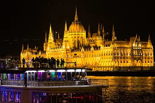 a party boat sailing by the lit up Parliament at night