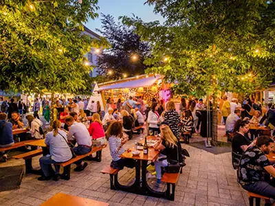 visitors sitting and eating at wooden tables at the Gourmet Festival in Millenaris park early evening in summer