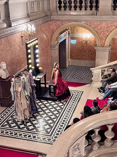 a female singer in a red costume performing an aria in the grand staircase of the Hungarian Opera House