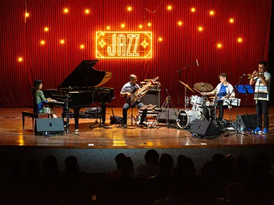 a jazz band playing a stage, The word"JAZZ" illuminated in yellow LED behind them on a red paneled wall