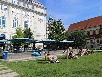 people lounging on the lawn and under the blue shades of Kiosk Terasz restaurant