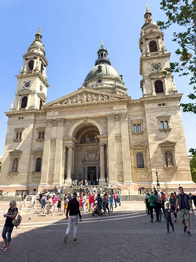 front view of the facade of St Stephen's Basilica on aclear sunny day, tourists mingling in the square in front of the church