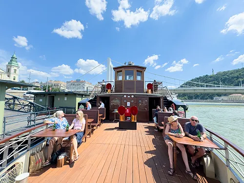 tourists on the vintage-style wooden open deck of the Kisfaludy historic steam boat on a slightly cloudy spring day