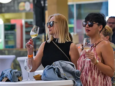 a blonde and a dark haired woman drinking white wine on a festival (in summer time)