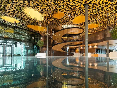 the stunning main hall of the House of Music in Budapest: golden, orange and yellow colored ceiling with black geometric patterns and a spiral staircase in the middle