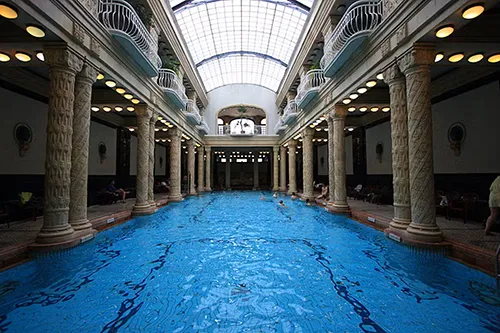 Indoor spa pool at Gellért Thermal Bath in Budapest, surrounded by intricate Art Nouveau columns and balconies beneath a vaulted glass ceiling.