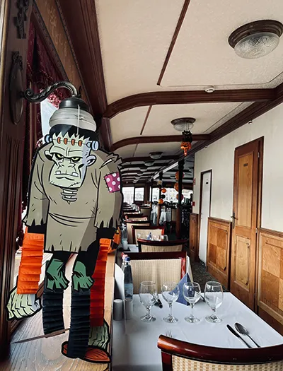 A cardboard cutout of Frankenstein's monster stands in the aisle of a dining boat, which is decorated with pumpkins and balloons for Halloween. The table settings are visible in the background. A cardboard cutout of Frankenstein's monster stands in the aisle of a dining boat, which is decorated with pumpkins and balloons for Halloween. The table settings are visible in the background.